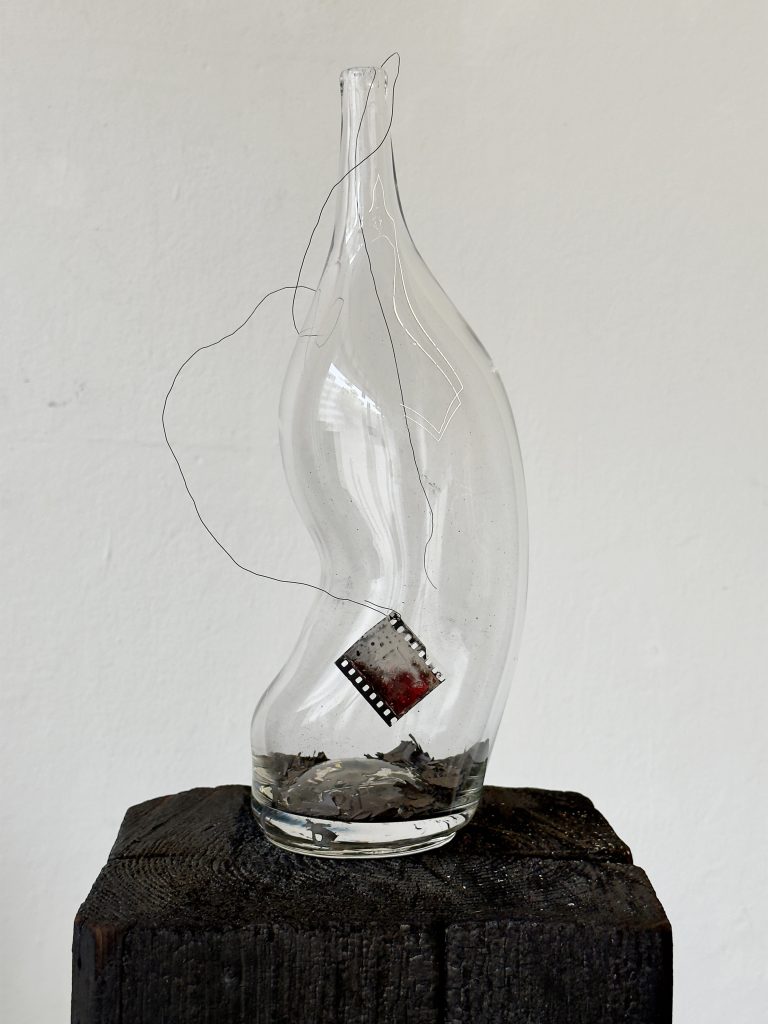 Henrik Strömberg, wishful send off 01, 2026 handblown glass bottle, burned newspaper, metal wire and overpainted film positive 38 x 15 x 15 cm