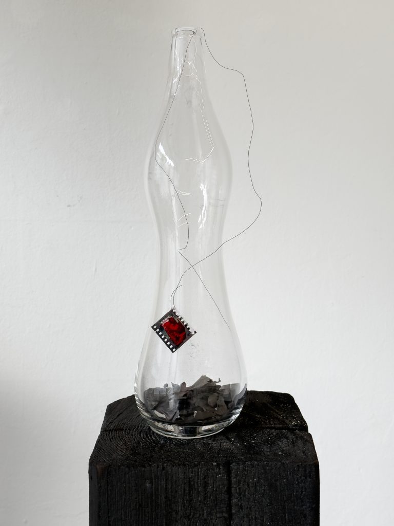 Henrik Strömberg, wishful send off 03, 2026 - handblown glass bottle, burned newspaper, metal wire and overpainted film positive 46 x 15 x 13 cm